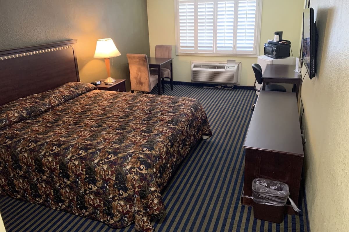 A hotel room with a bed, a desk, a chair, an air conditioner, and a television.