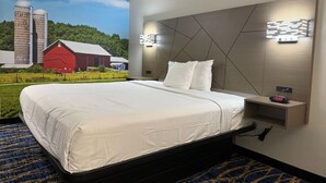 A hotel room with a large bed, a headboard with geometric patterns, a bedside table with a clock, and a mural of a farm scene. - Travelodge by Wyndham Odessa (Odessa)
