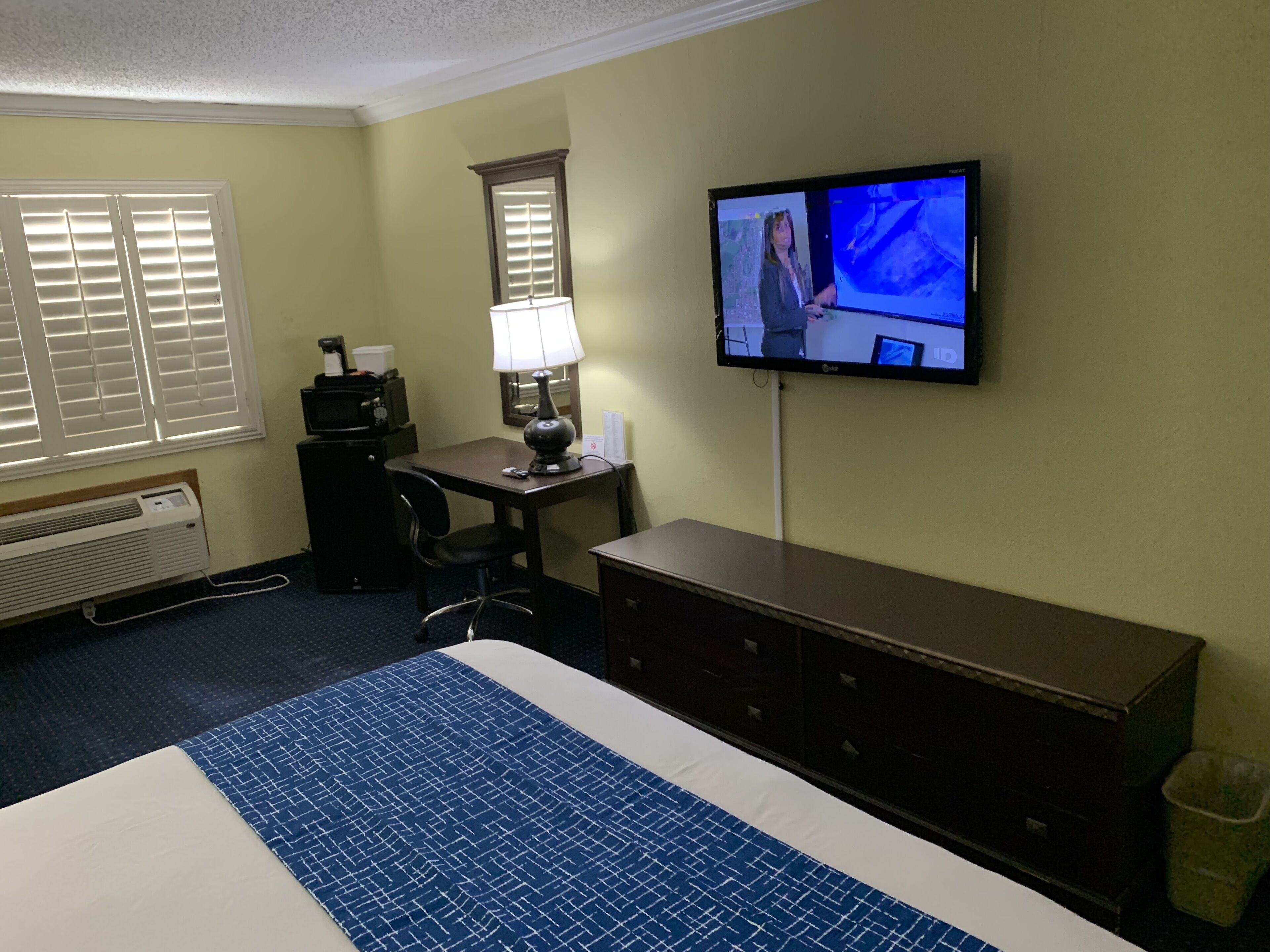 Een hotelkamer met een groot bed, een bureau met lamp, een aan de muur bevestigde televisie en een prullenbak.