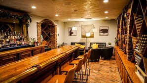 A bar area with a long wooden counter, multiple stools, and a brick wall backdrop. - Historic Santa Maria Inn (Santa Maria)