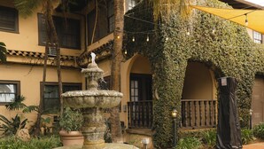 A courtyard with a stone fountain, palm trees, and a building with ivy-covered arches. - Historic Santa Maria Inn (Santa Maria)
