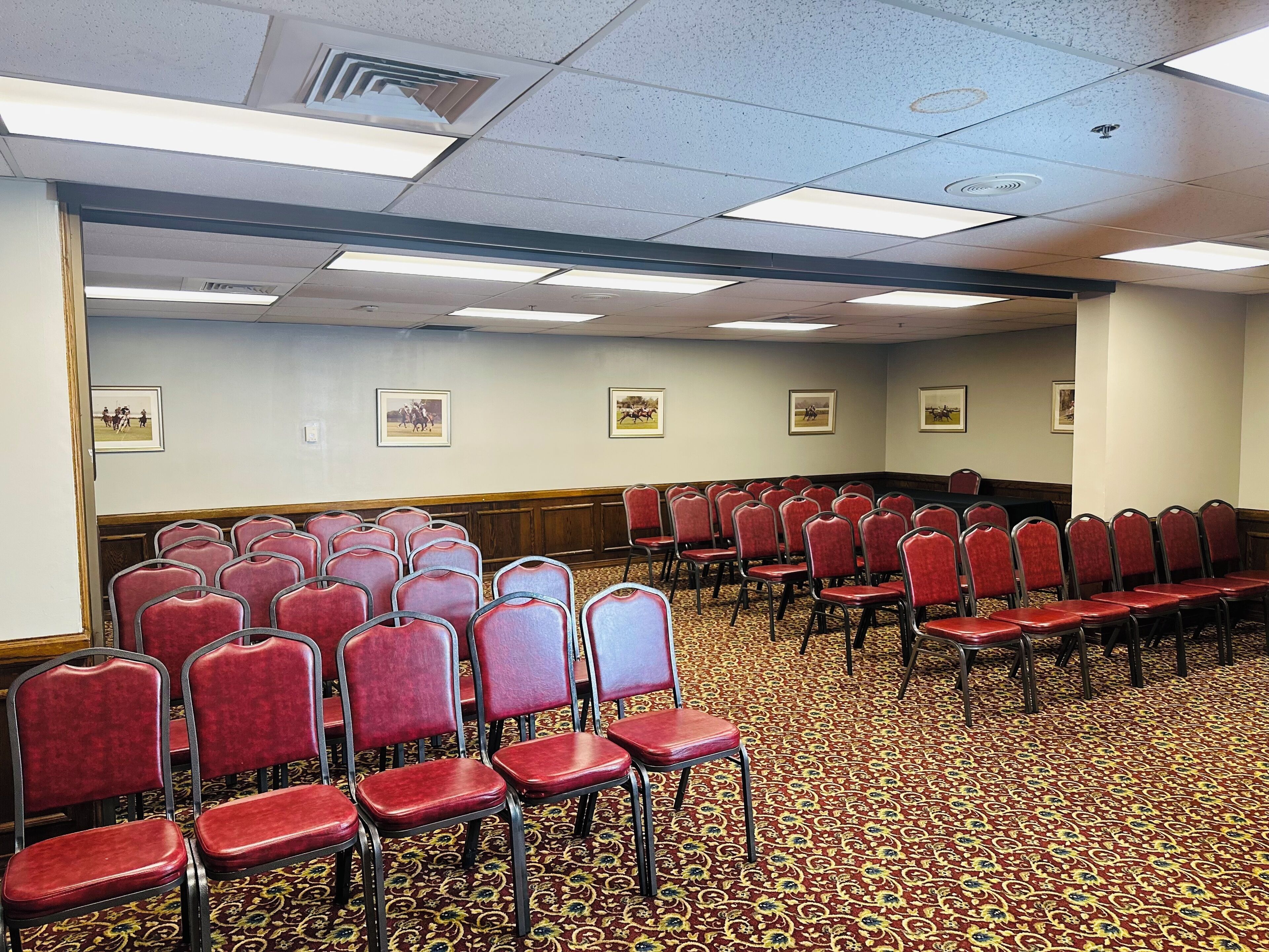 A conference room with rows of red chairs, carpeted floor, and ceiling lights.