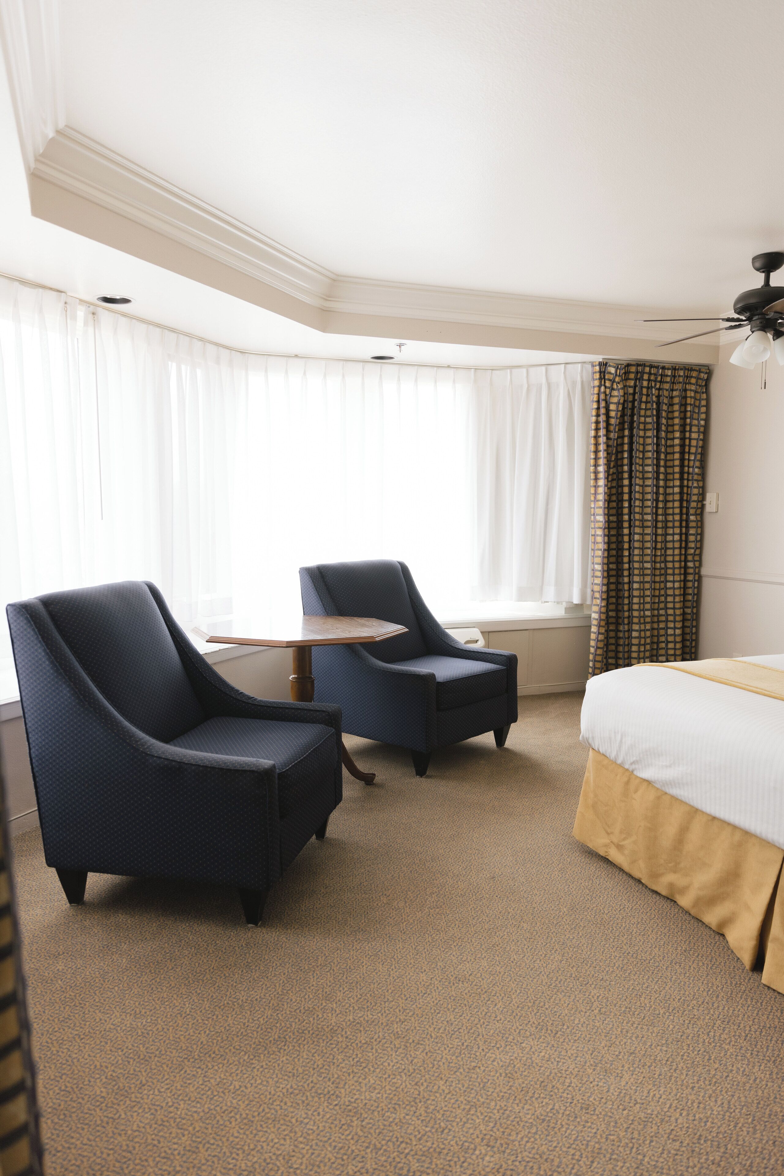 A hotel room with two armchairs, a small table, a bed, and a window with curtains.