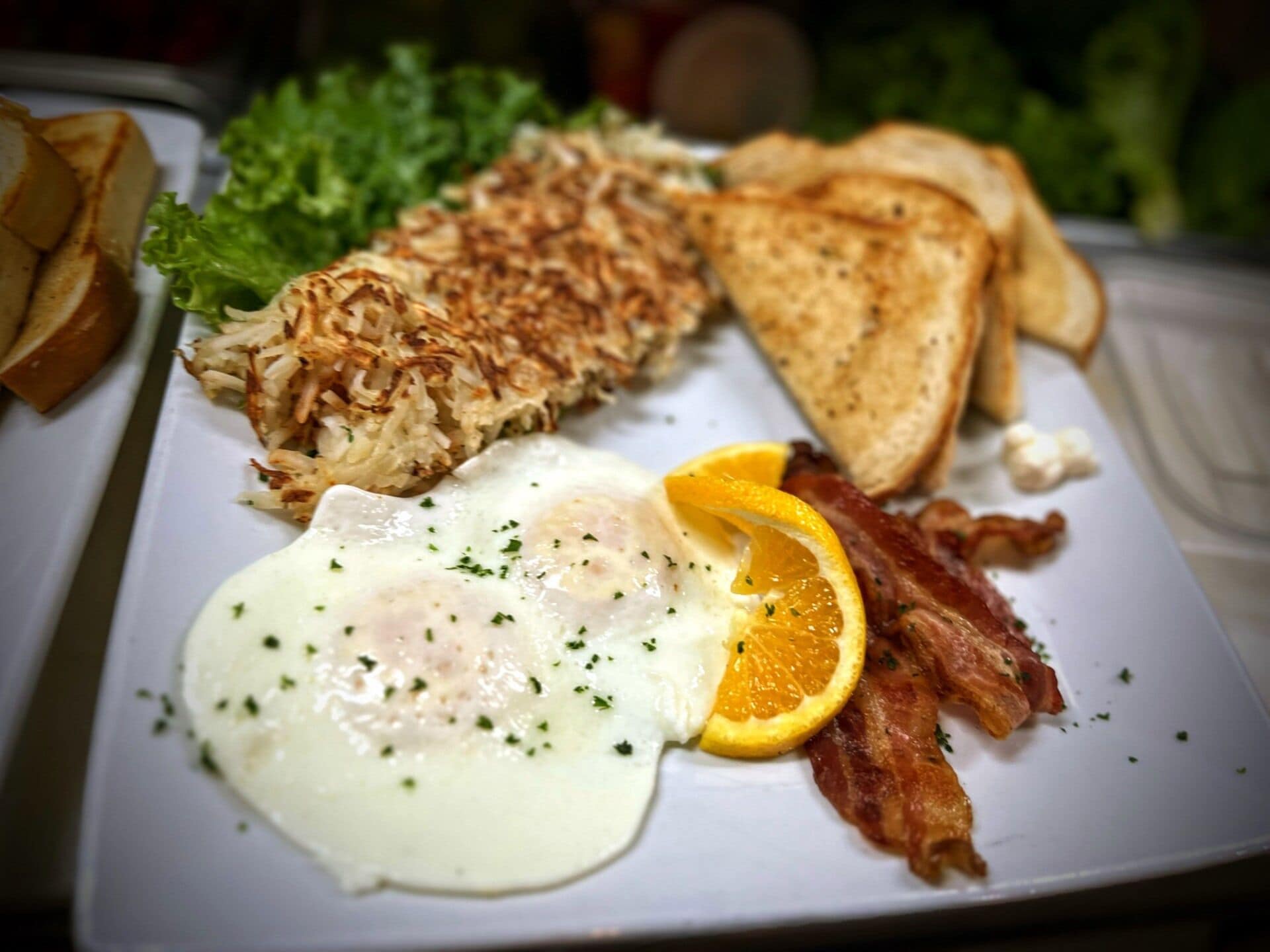 A plate with eggs, bacon, toast, hash browns, and a slice of orange.