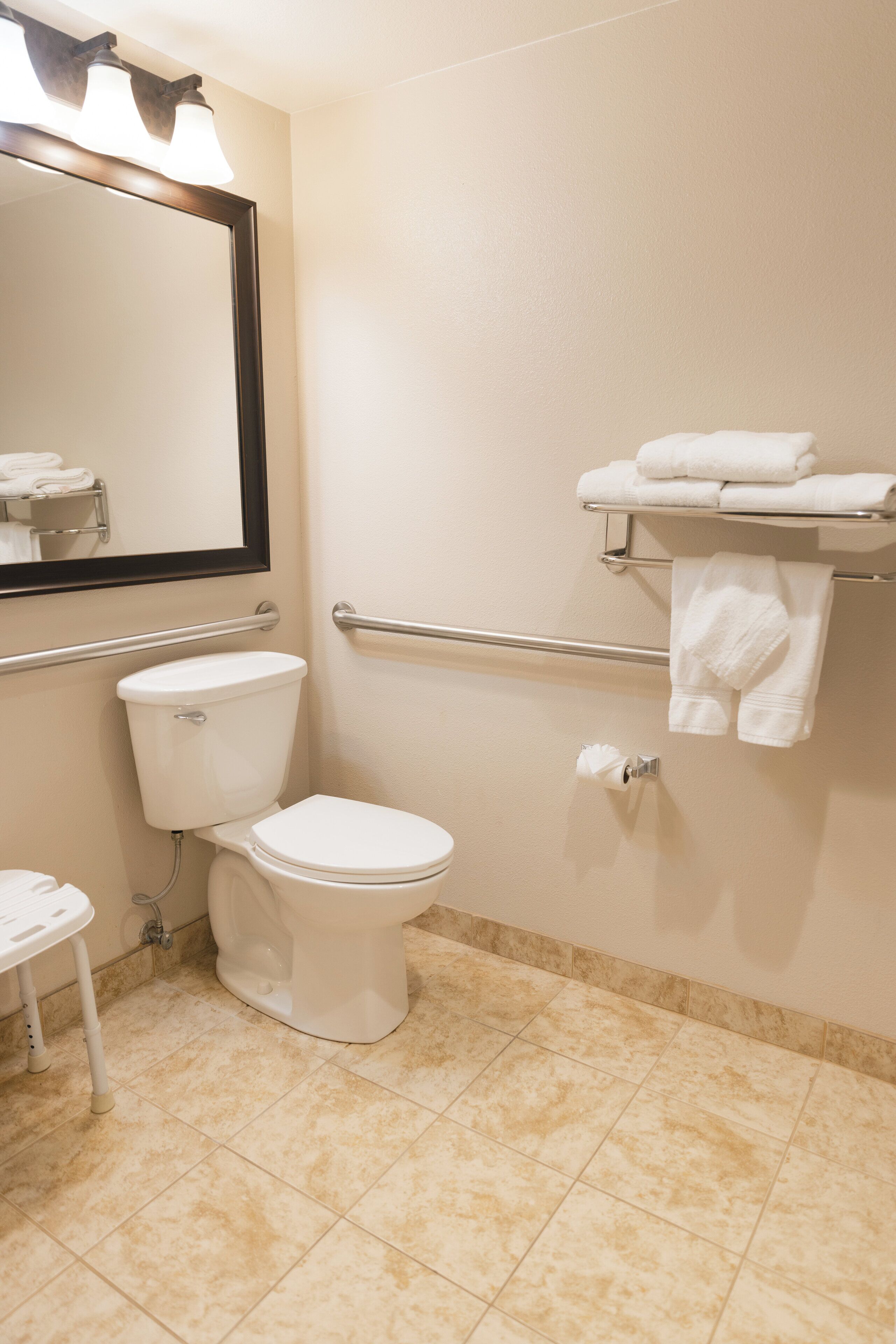 Un baño con inodoro, lavamanos, espejo y toallero con toallas.