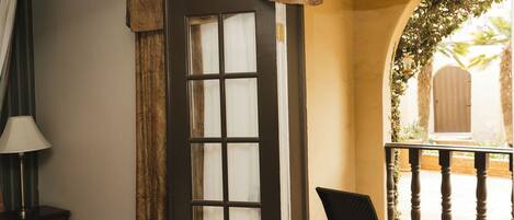 A hotel room with a bed, a chair, a door leading to an outdoor area, and a lamp.