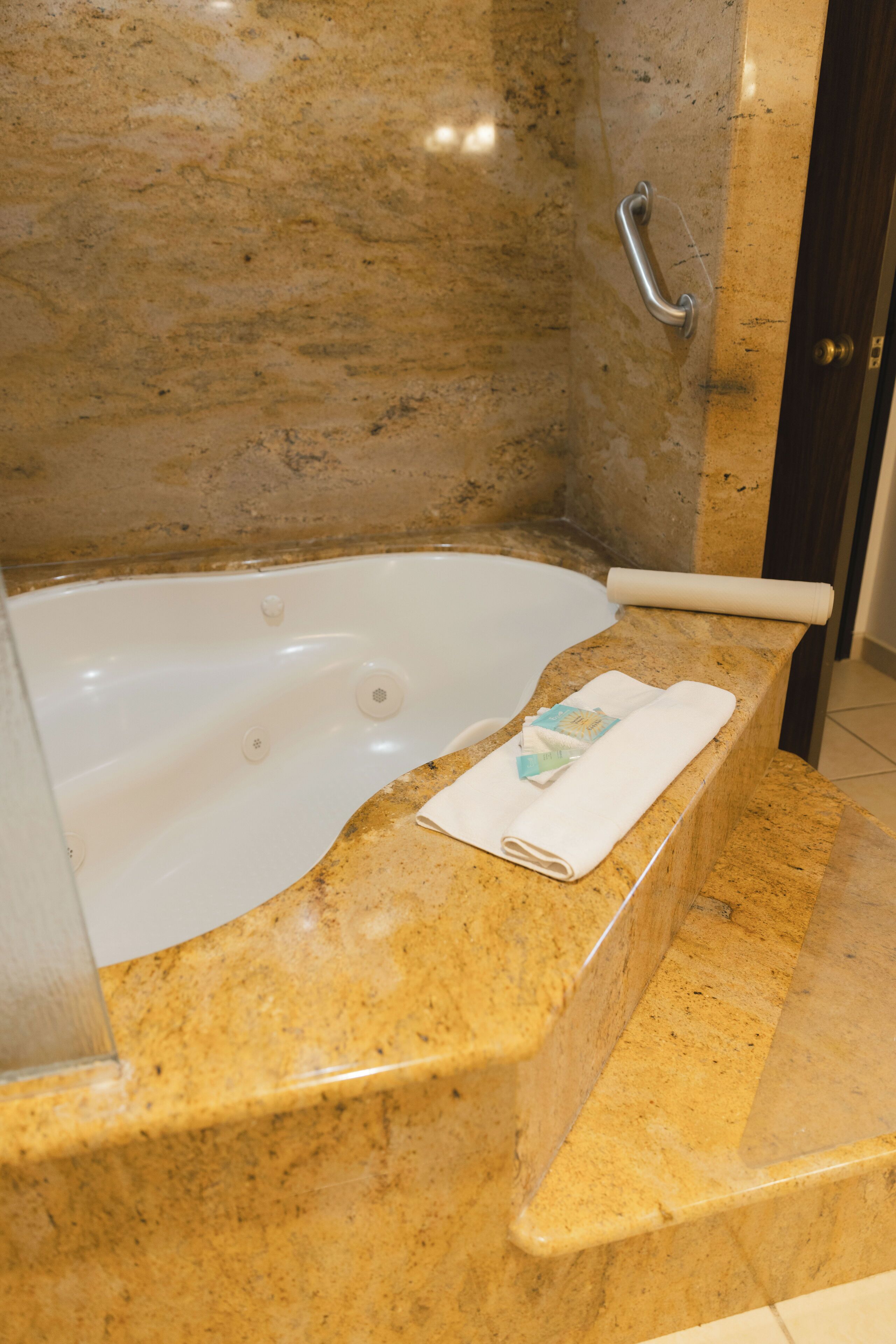 Un baño de mármol con una bañera, una toalla y un barandal.