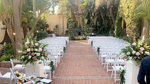 An outdoor wedding venue with rows of white chairs and floral centerpieces. - Historic Santa Maria Inn (Santa Maria)