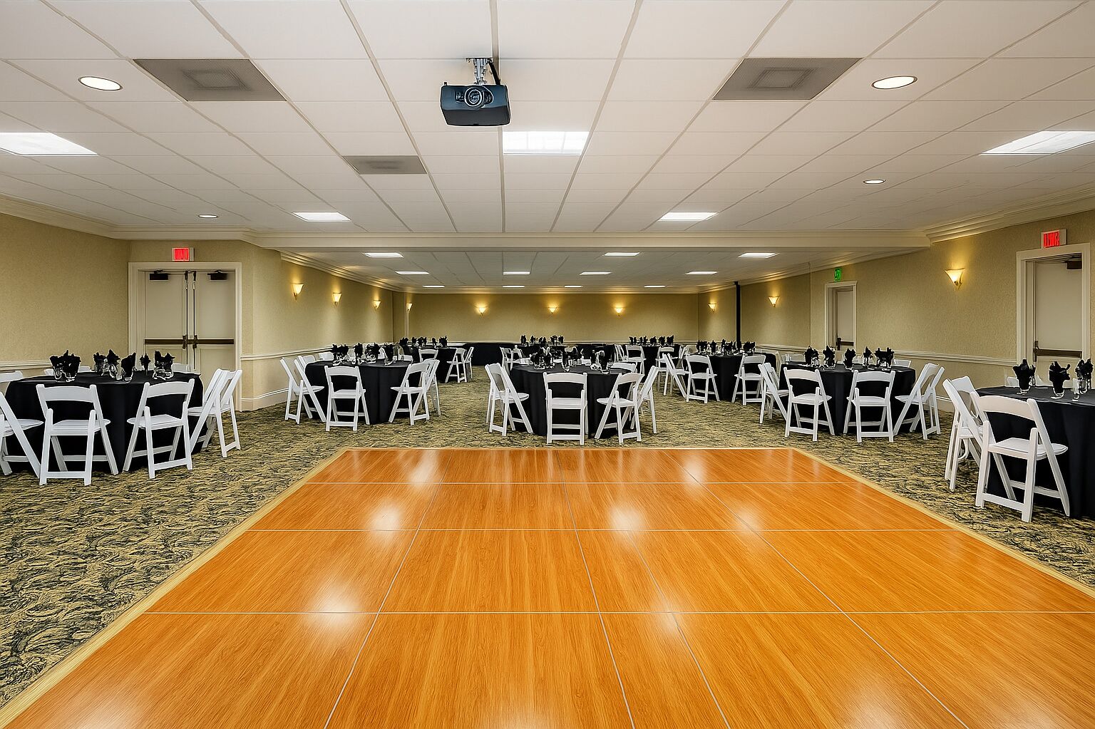 A conference room with multiple tables and chairs, a wooden floor, and a projector mounted on the ceiling.