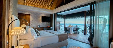 A bedroom with a bed, bedside table, lamp, and a view of the ocean.