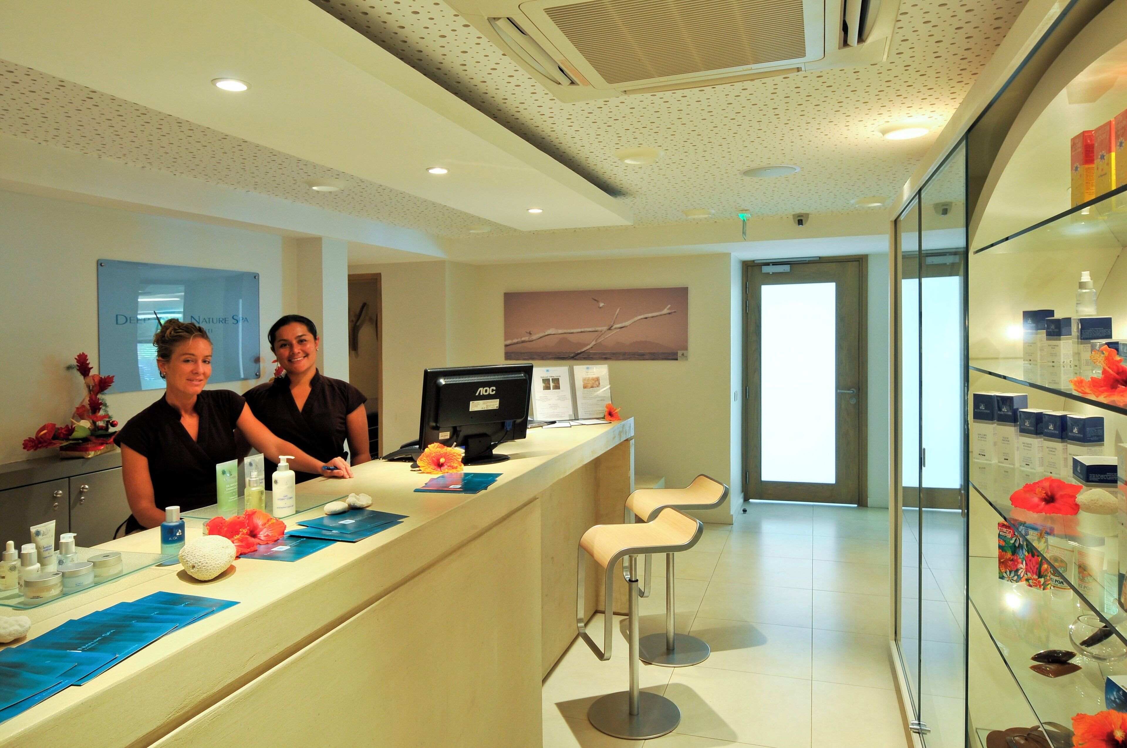 A reception area with a counter, two receptionists, a computer, and a glass display case with products.
