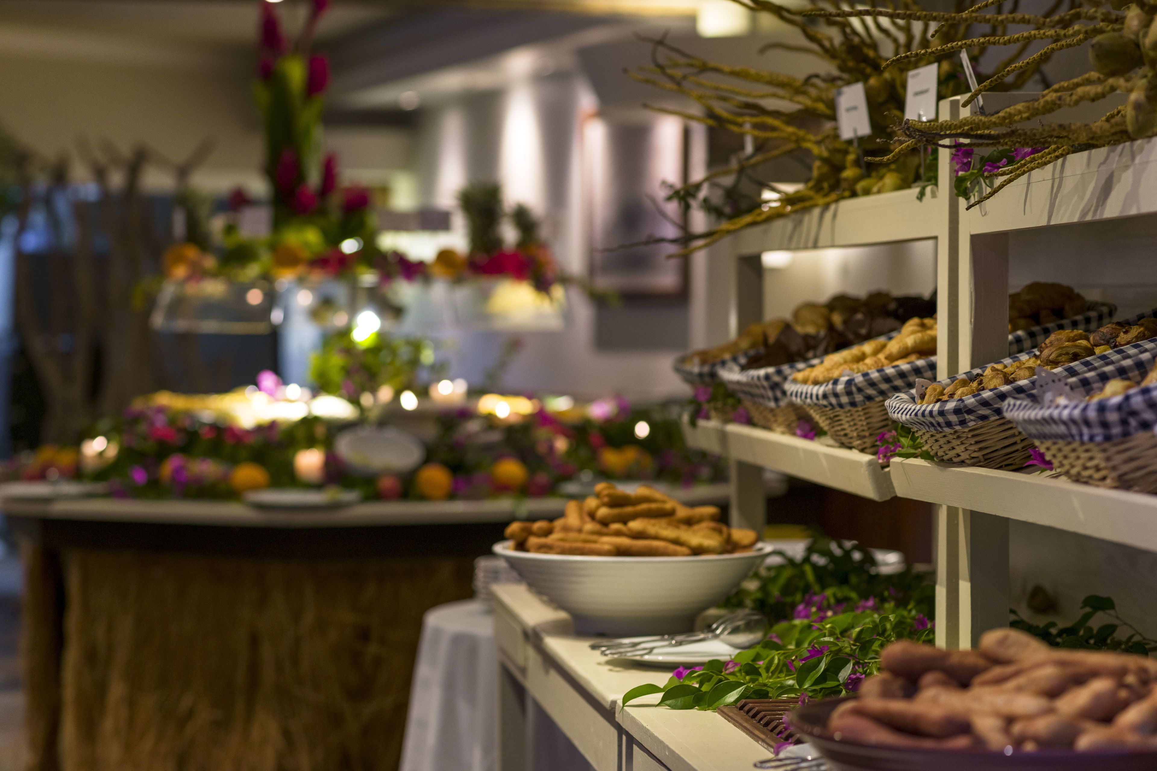 A buffet table with various food items and baskets, surrounded by decorative plants and candles.