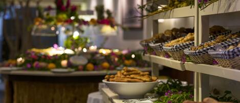 A buffet table with various food items and baskets, surrounded by decorative plants and candles.