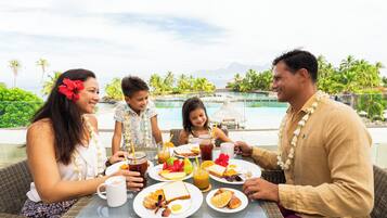 A family dining at a table with a view of a pool and mountains.