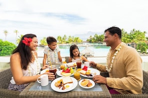 A family dining at a table with a view of a pool and mountains.