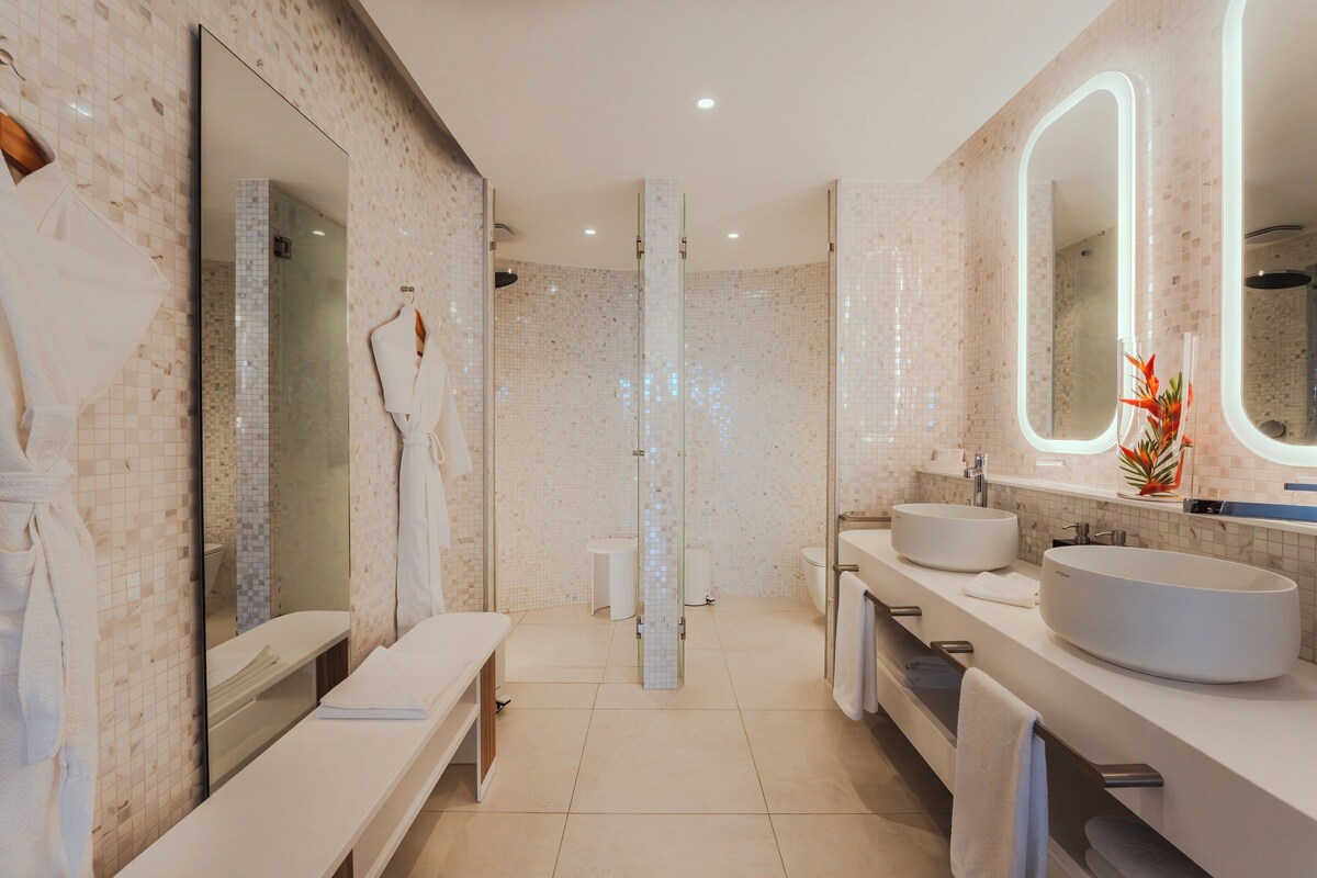 Une salle de bain moderne avec deux lavabos, un grand miroir et un banc.