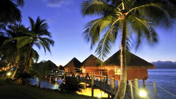 A resort with overwater bungalows, palm trees, and a view of the ocean.