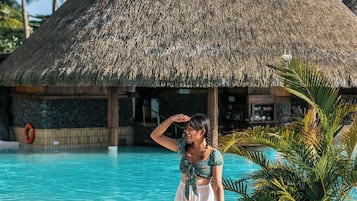 A resort with a thatched-roof structure, a swimming pool, and palm trees.
