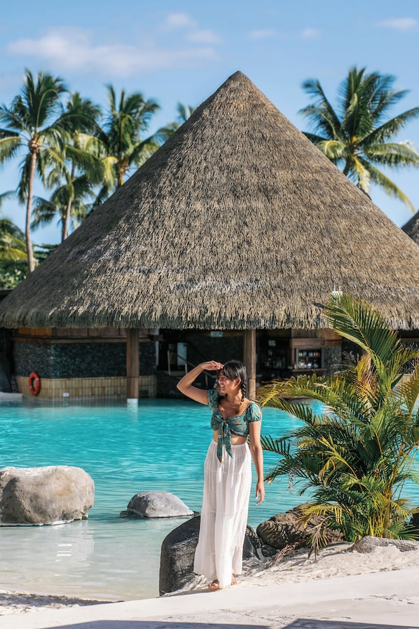 A resort with a thatched-roof structure, a swimming pool, and palm trees.