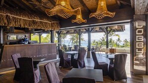 A restaurant with a bar, outdoor seating, and a view of the ocean.