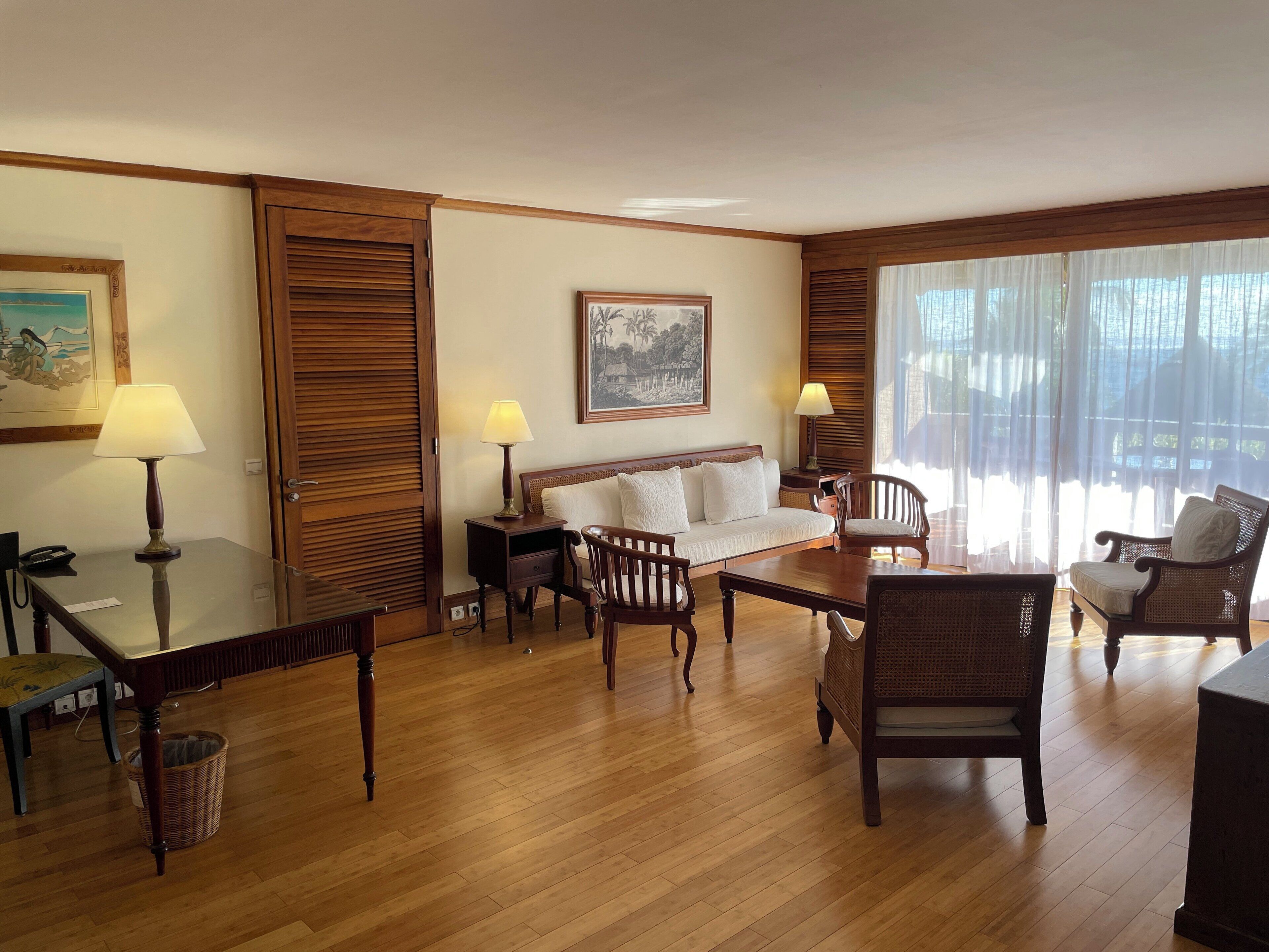A hotel room with a wooden floor, a sofa, two chairs, a table, and a lamp.