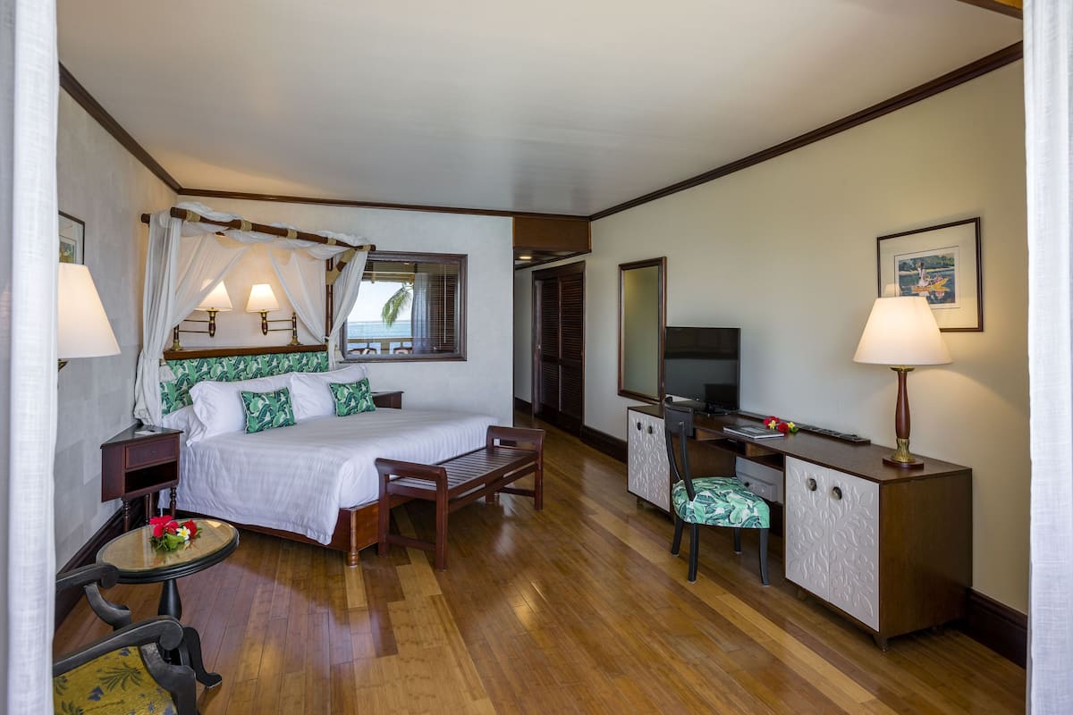 A hotel room with a bed, bedside table, lamp, desk, chair, and a TV.