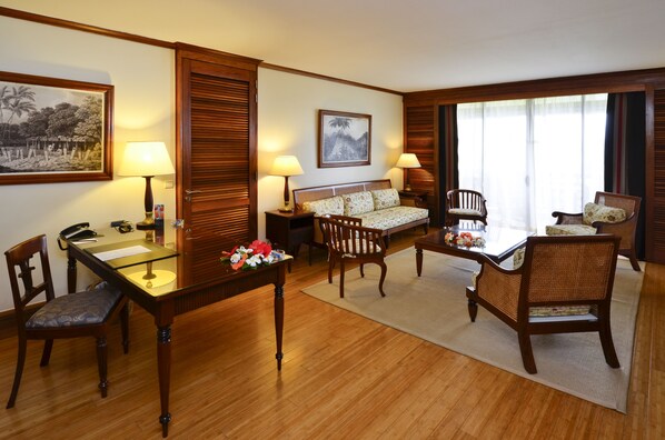 A hotel room with a wooden floor, a dining table with chairs, a sofa, and two lamps.