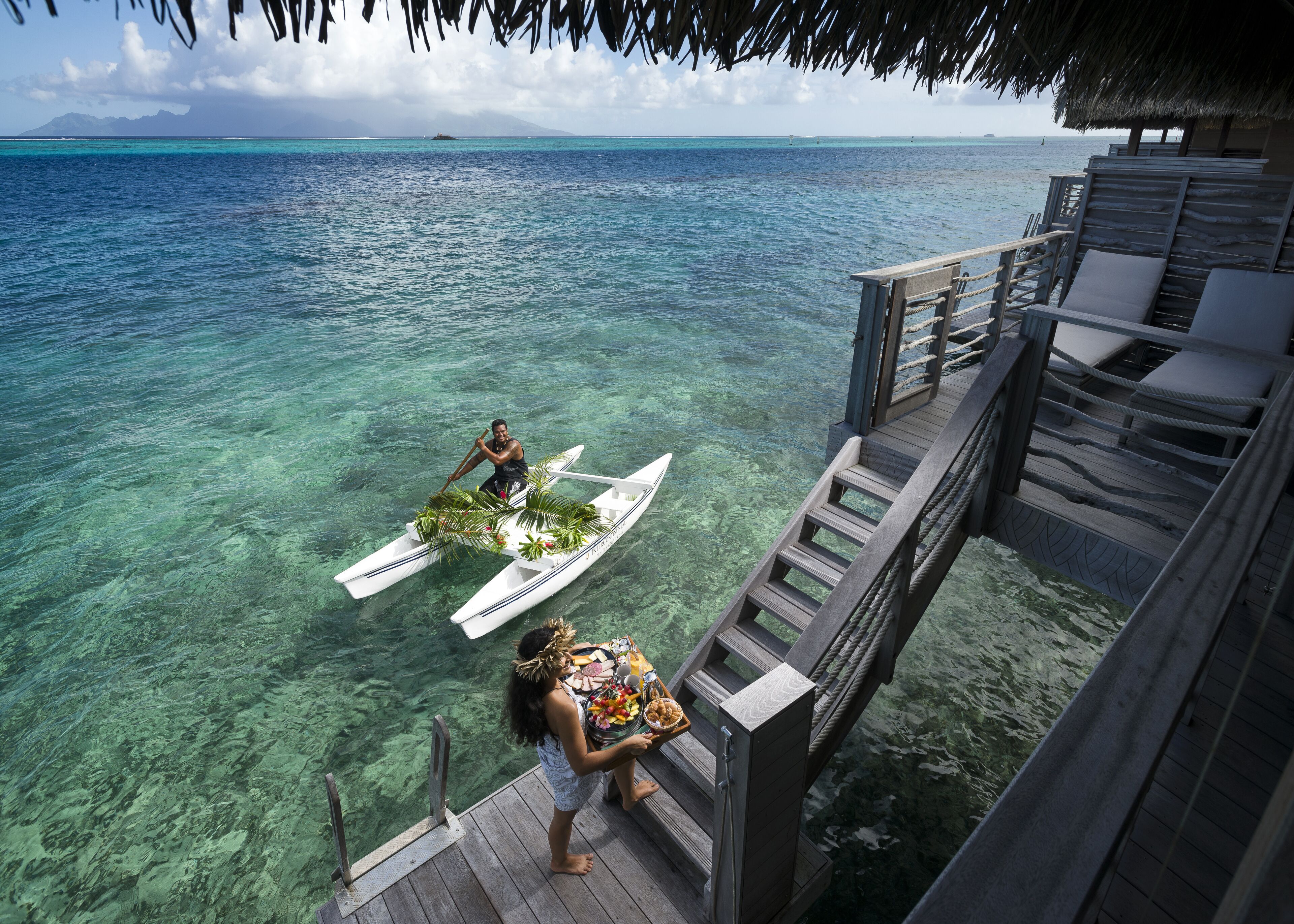 A wooden deck with a thatched roof, overlooking clear turquoise waters.