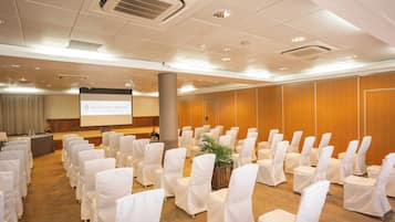 A conference room with rows of white-covered chairs, a podium, and a presentation screen.