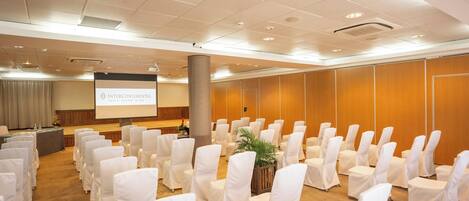 A conference room with rows of white-covered chairs, a podium, and a presentation screen.