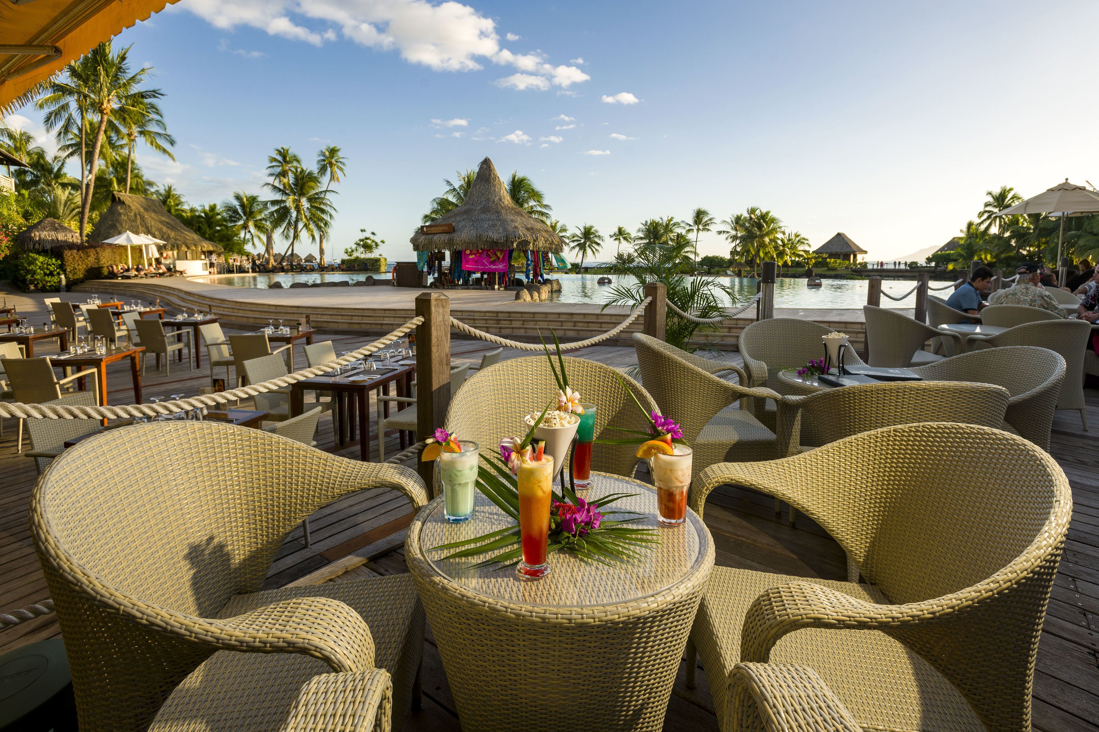 A tropical resort with wicker furniture, a pool, and palm trees.
