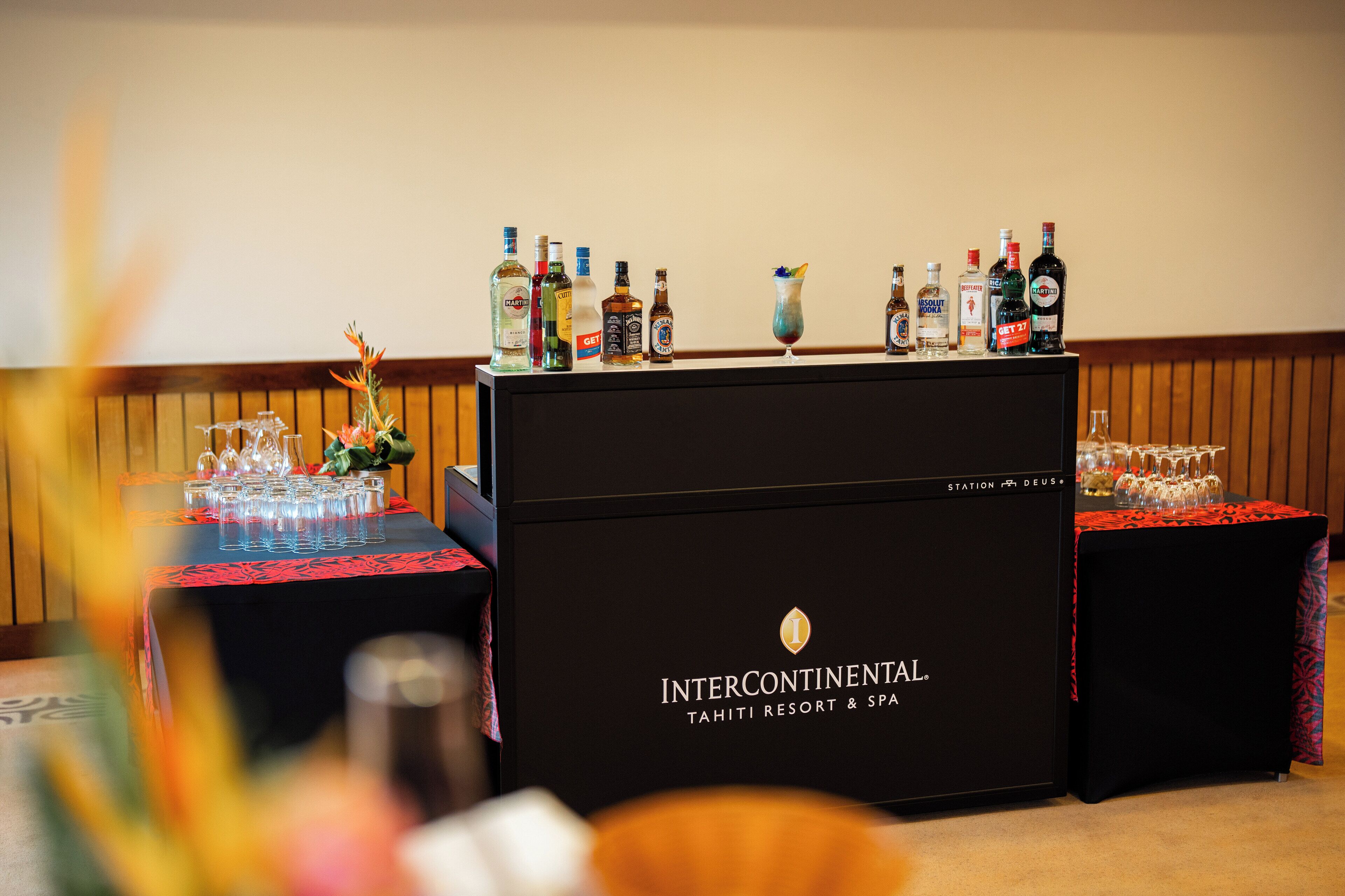 Uma área de bar com diversas garrafas de bebidas e copos, um balcão preto com o logotipo InterContinental e uma toalha de mesa vermelha.