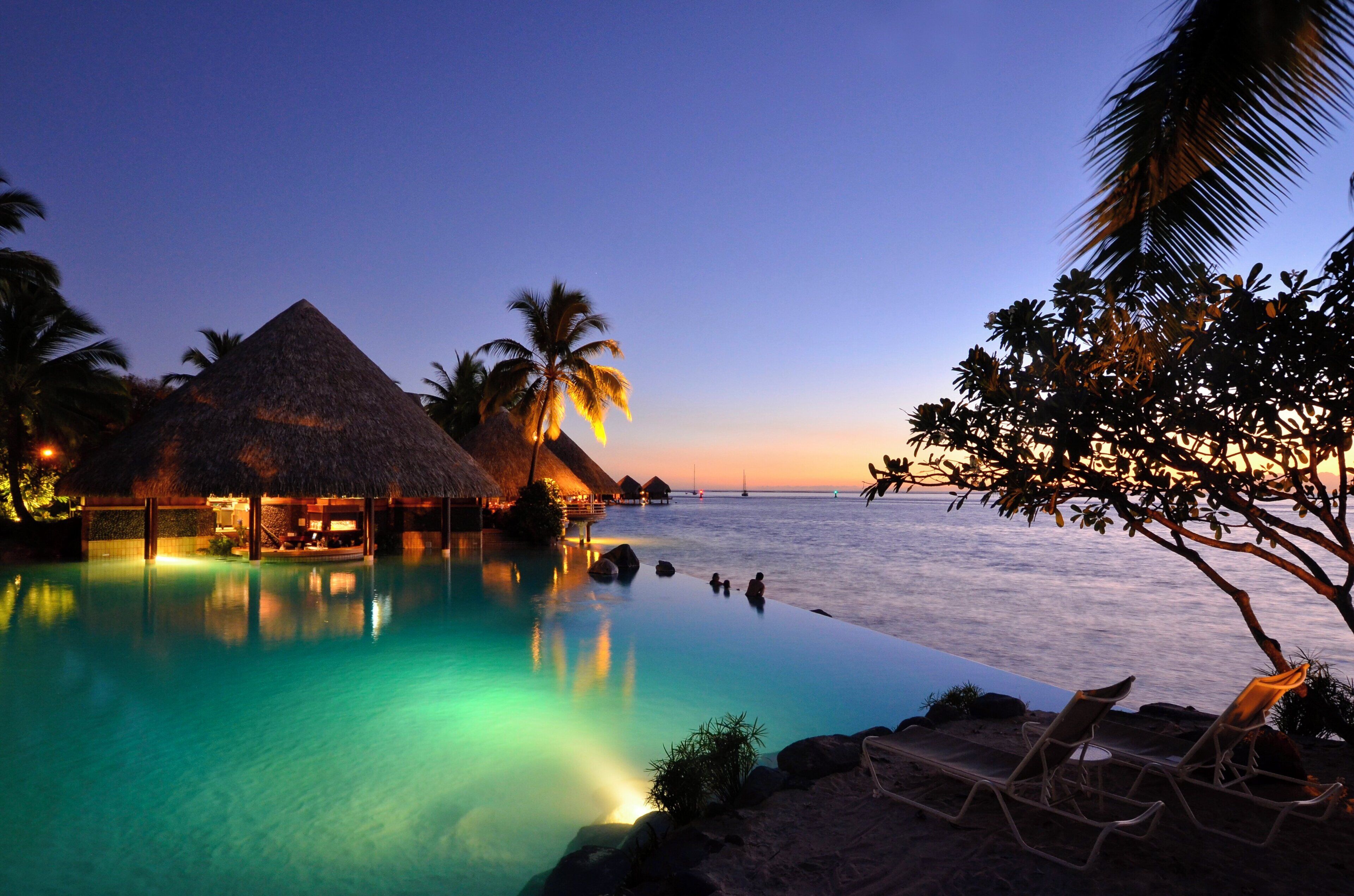 A resort with a swimming pool, overwater bungalows, and a beach area.