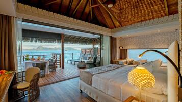 A bedroom with a bed, bedside table, lamp, and a view of the sea.