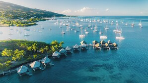 An aerial view of a coastal area with numerous sailboats and overwater bungalows.