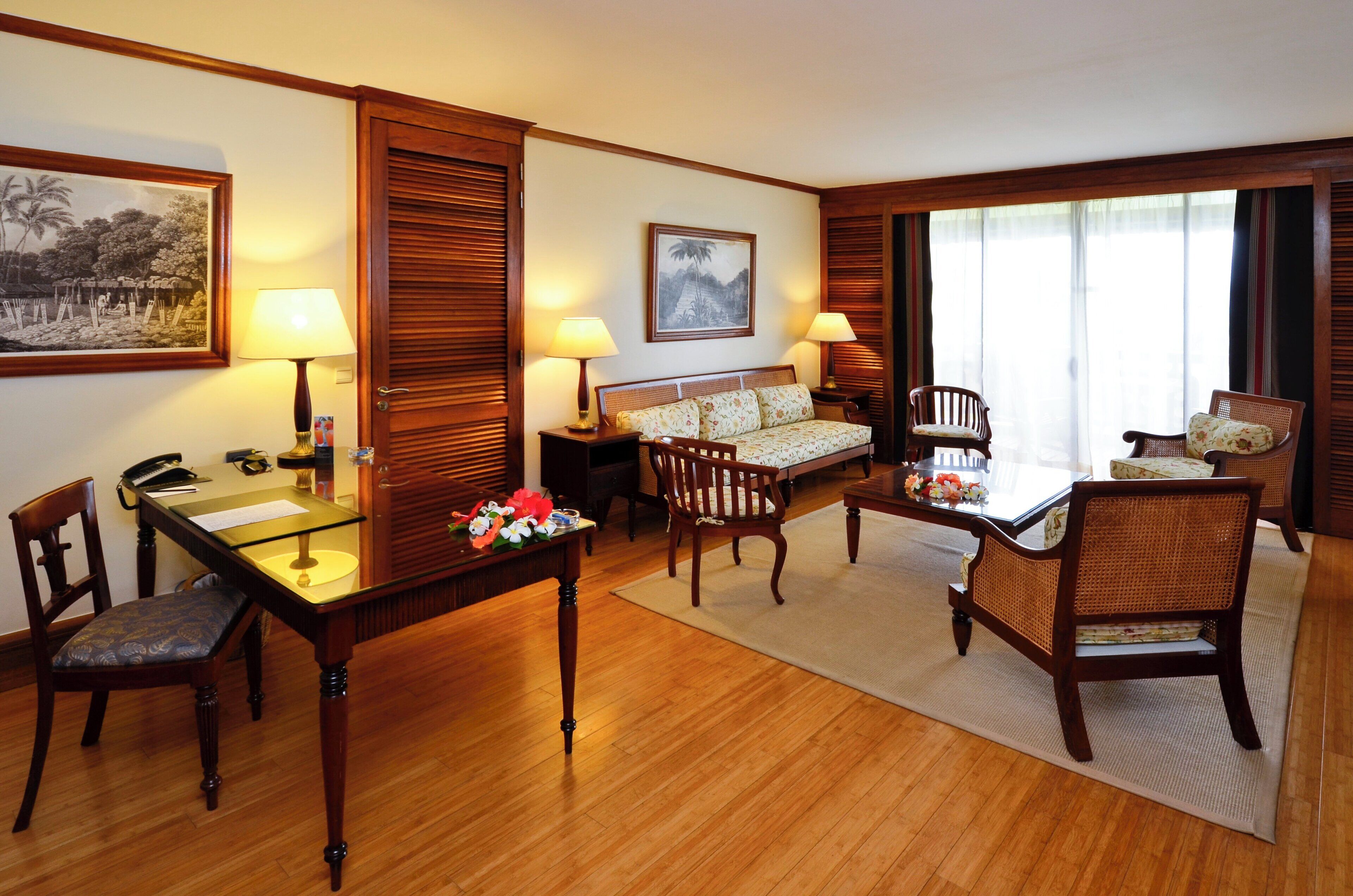 Ein Hotelzimmer mit Holzboden, einem Esstisch mit Stühlen, einer Couch, einem Schreibtisch mit Lampe und einem Bett mit Kopfteil.