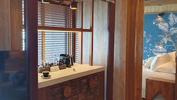 A room with a wooden counter, a coffee machine, and a view of a tropical scene through the window.