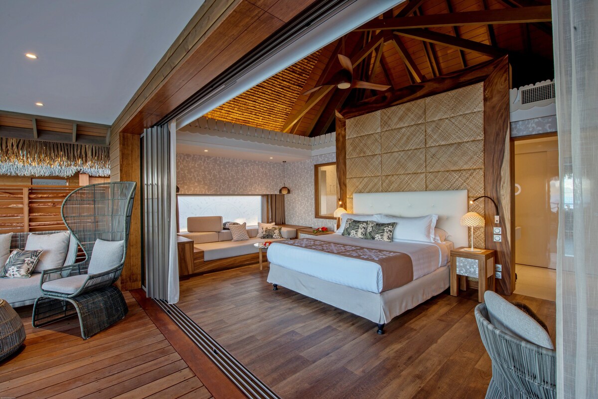Une chambre spacieuse avec un grand lit, un coin salon avec un canapé et des fauteuils, et un plafond en bois.