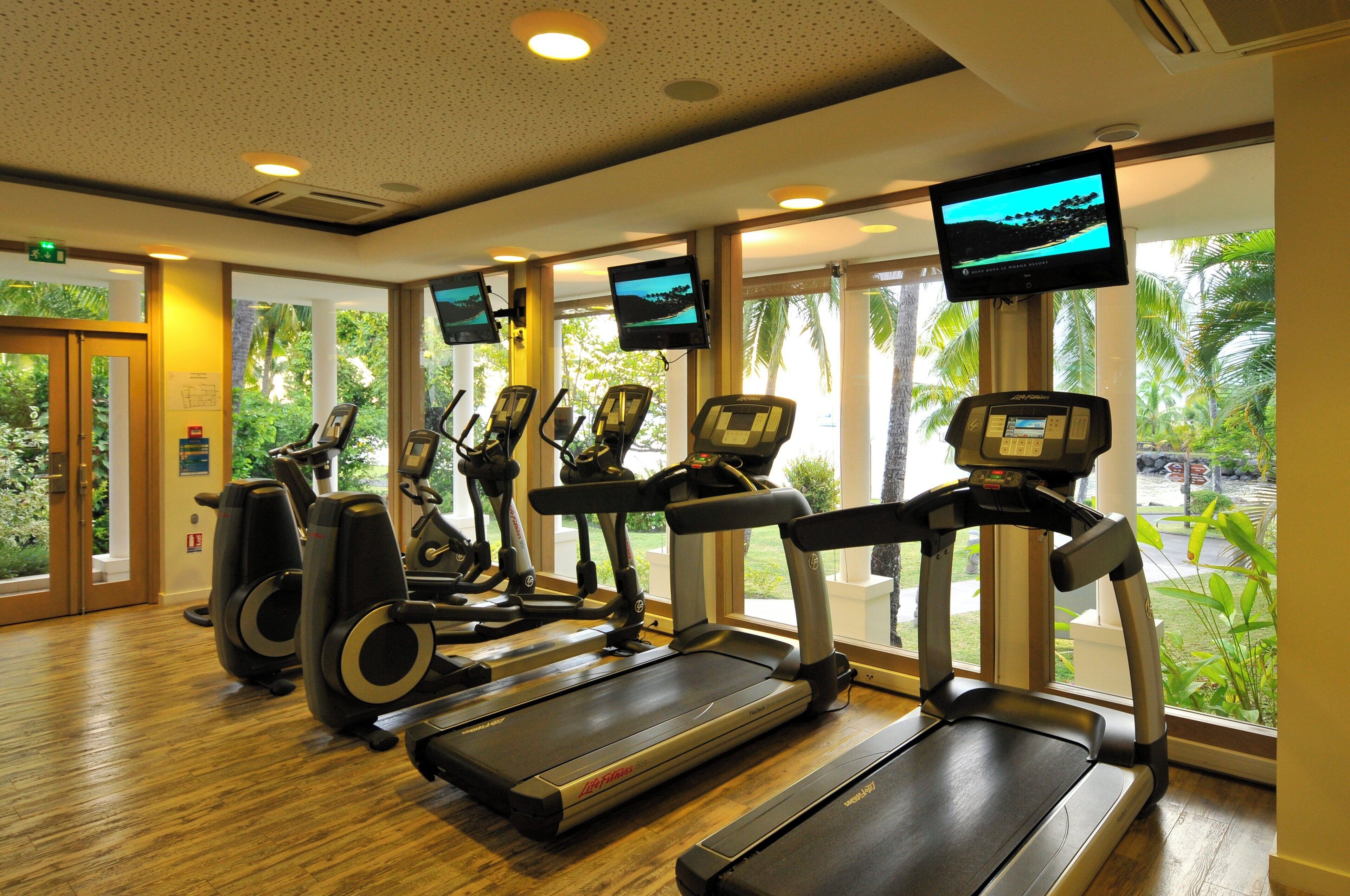A fitness center with treadmills, stationary bikes, and elliptical machines, equipped with digital screens.