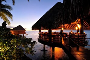 An overwater bungalows with thatched roofs, wooden deck, and dining area with tables and chairs. - InterContinental Resort Tahiti by IHG (Faaa)