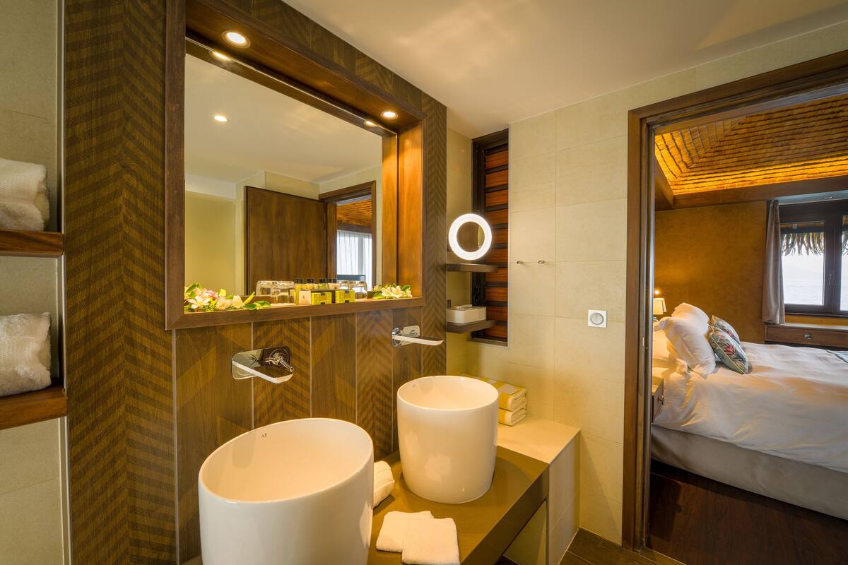 A modern bathroom with two large sinks, a mirror, and a bed with a view of the outdoors.