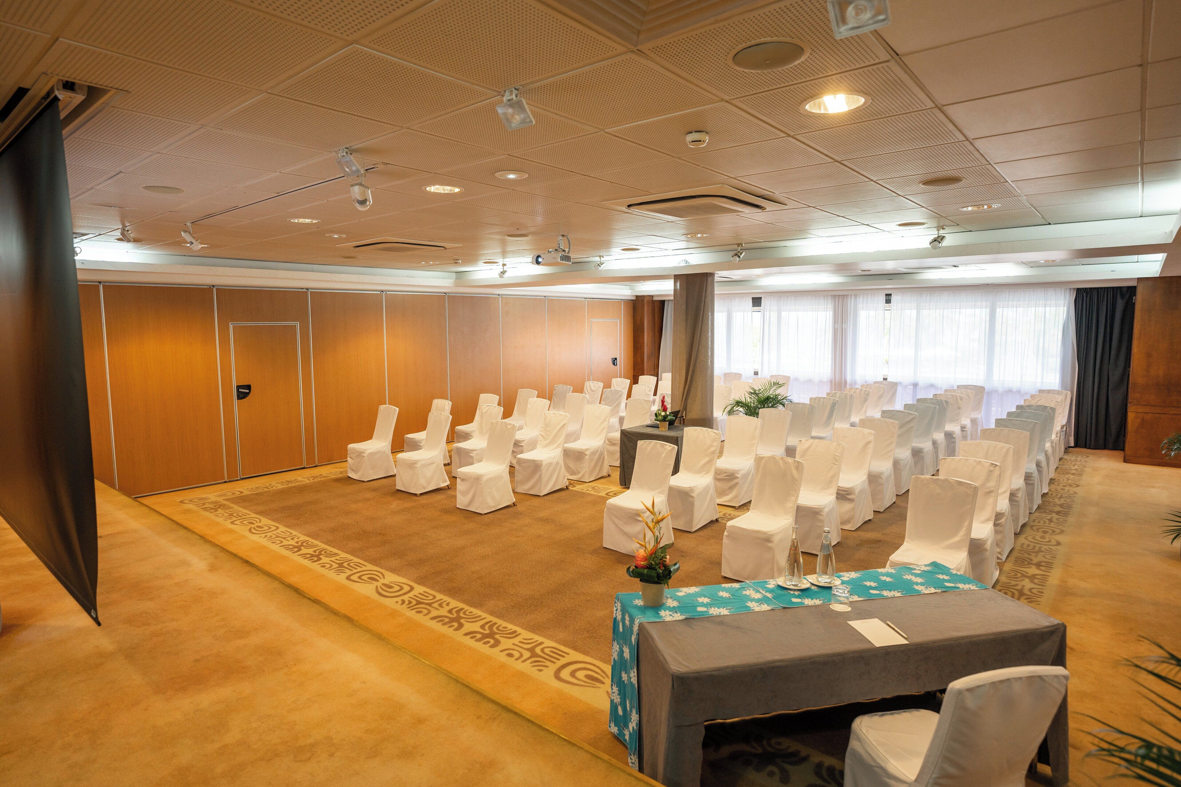 A conference room with rows of white chairs, a table with a blue tablecloth, and a carpeted floor.