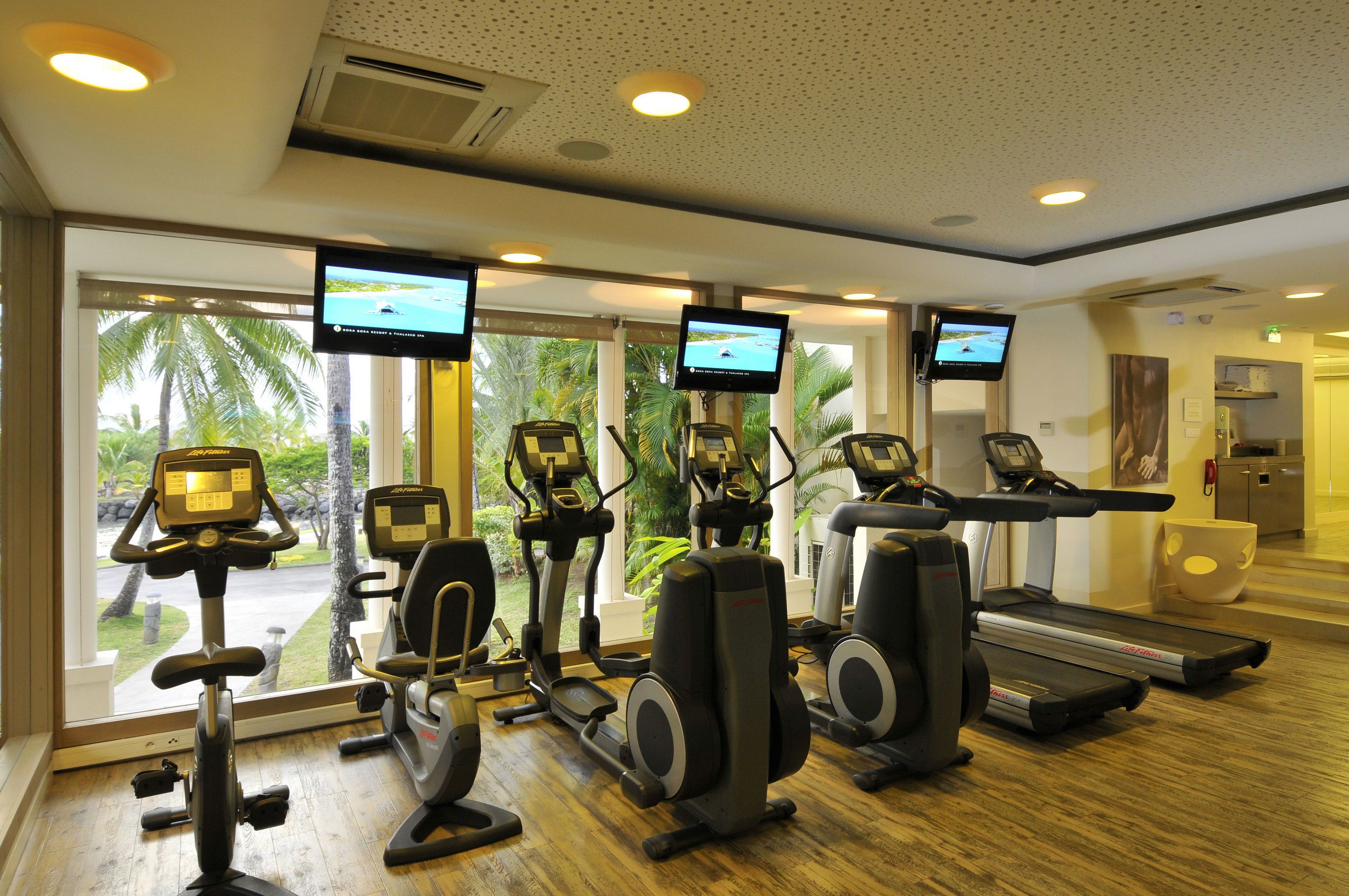 Une salle de sport équipée de tapis de course, de vélos elliptiques et de vélos d’appartement, dotée de grandes fenêtres et de plusieurs écrans.