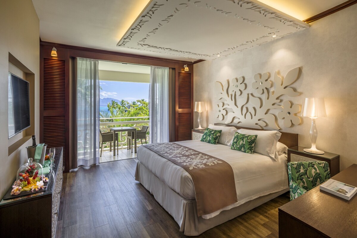 Une chambre d’hôtel comprenant un lit, une télévision, un balcon avec vue et un coin repas avec une table et des chaises.