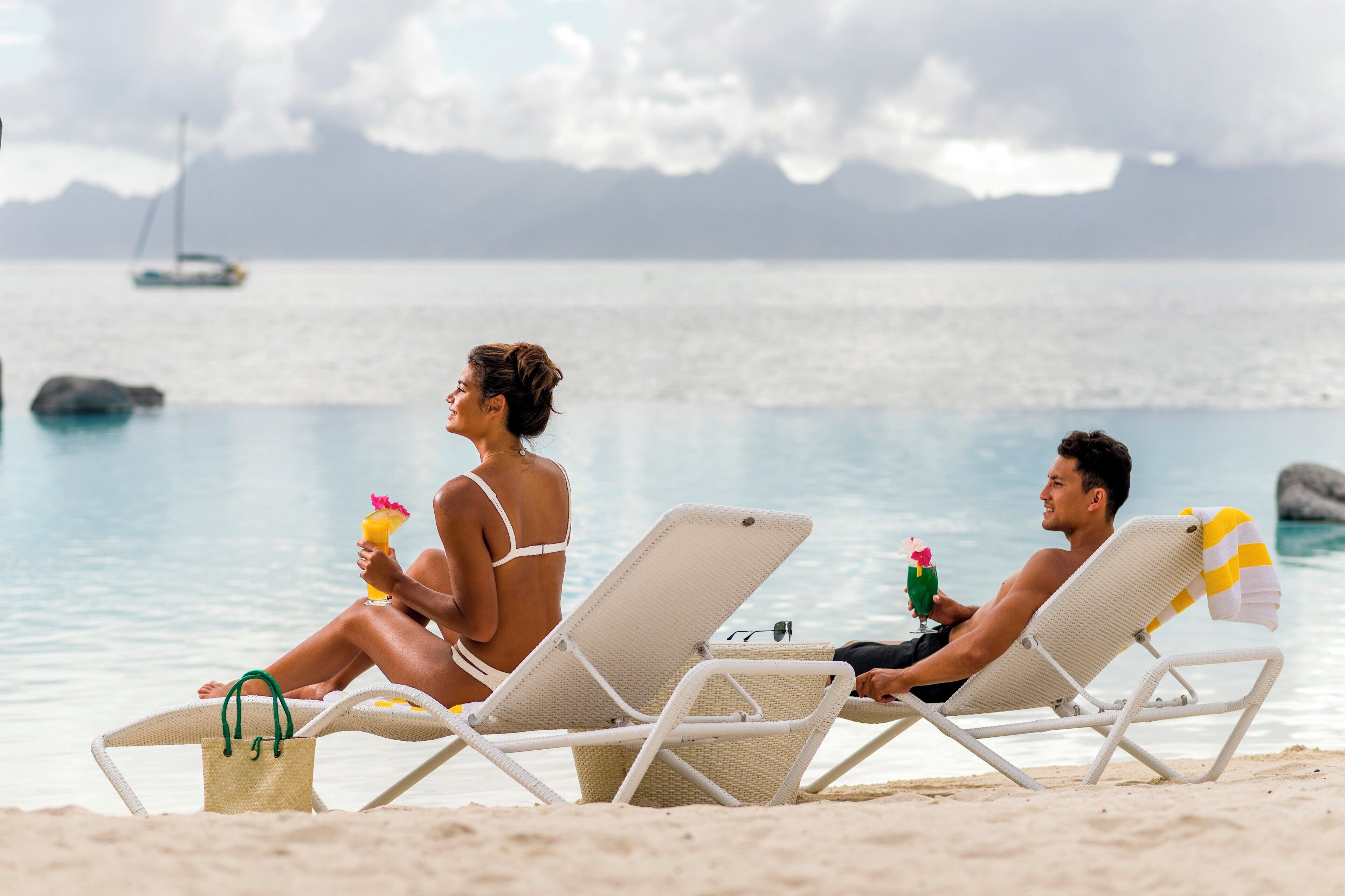 Two people sitting on beach chairs by the water, holding drinks.