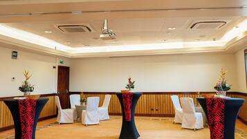 A conference room with a projector, tables with white chairs, and a patterned carpet.