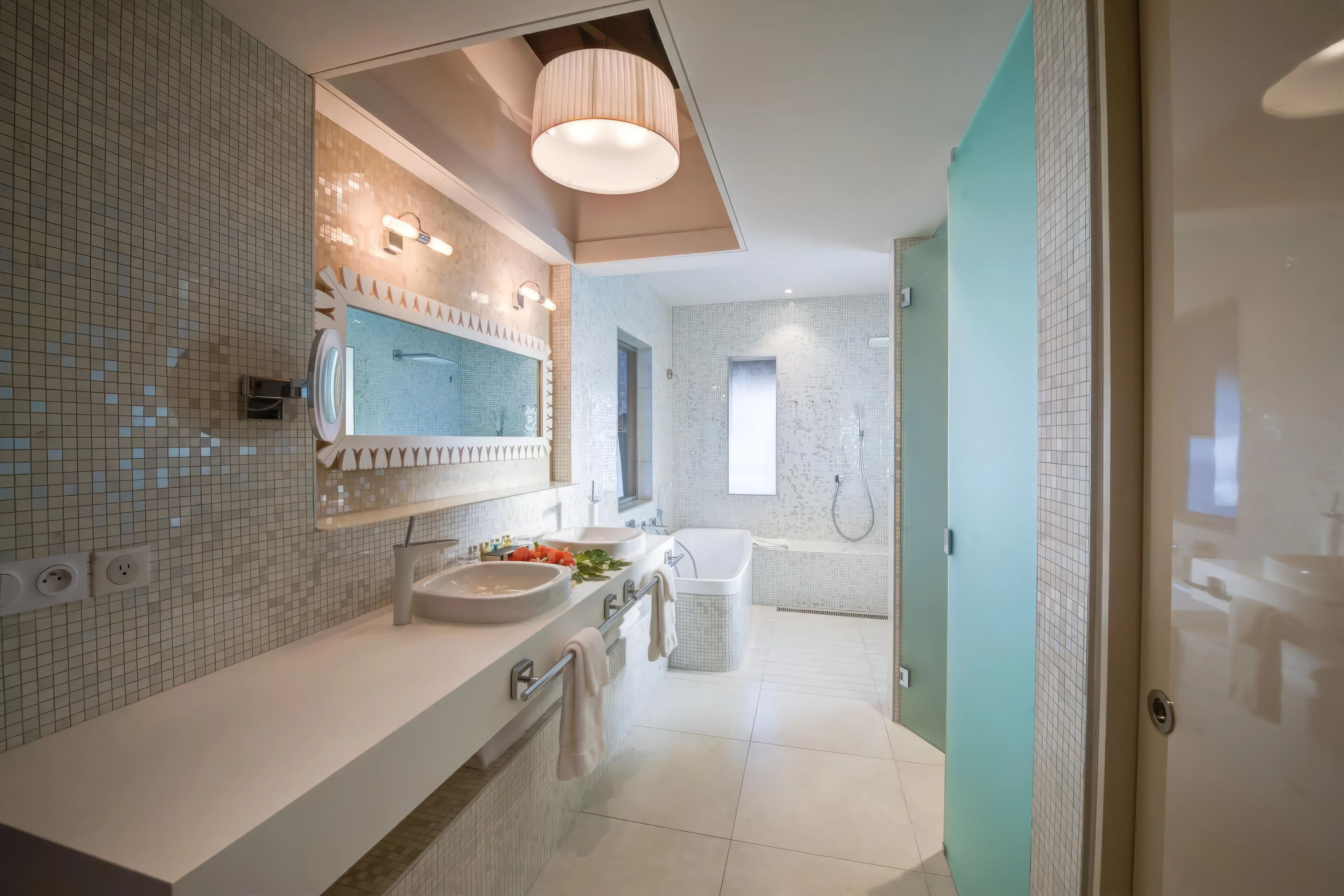 A modern bathroom with a large mirror, two sinks, a bathtub, and a shower.