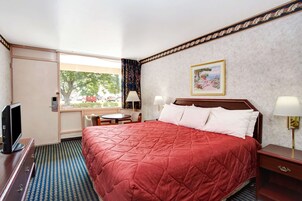 Habitación de hotel con una cama grande, televisión, escritorio con silla y ventana con cortinas.