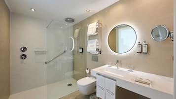 A modern bathroom with a glass-enclosed shower, a white sink, a toilet, and a round mirror.