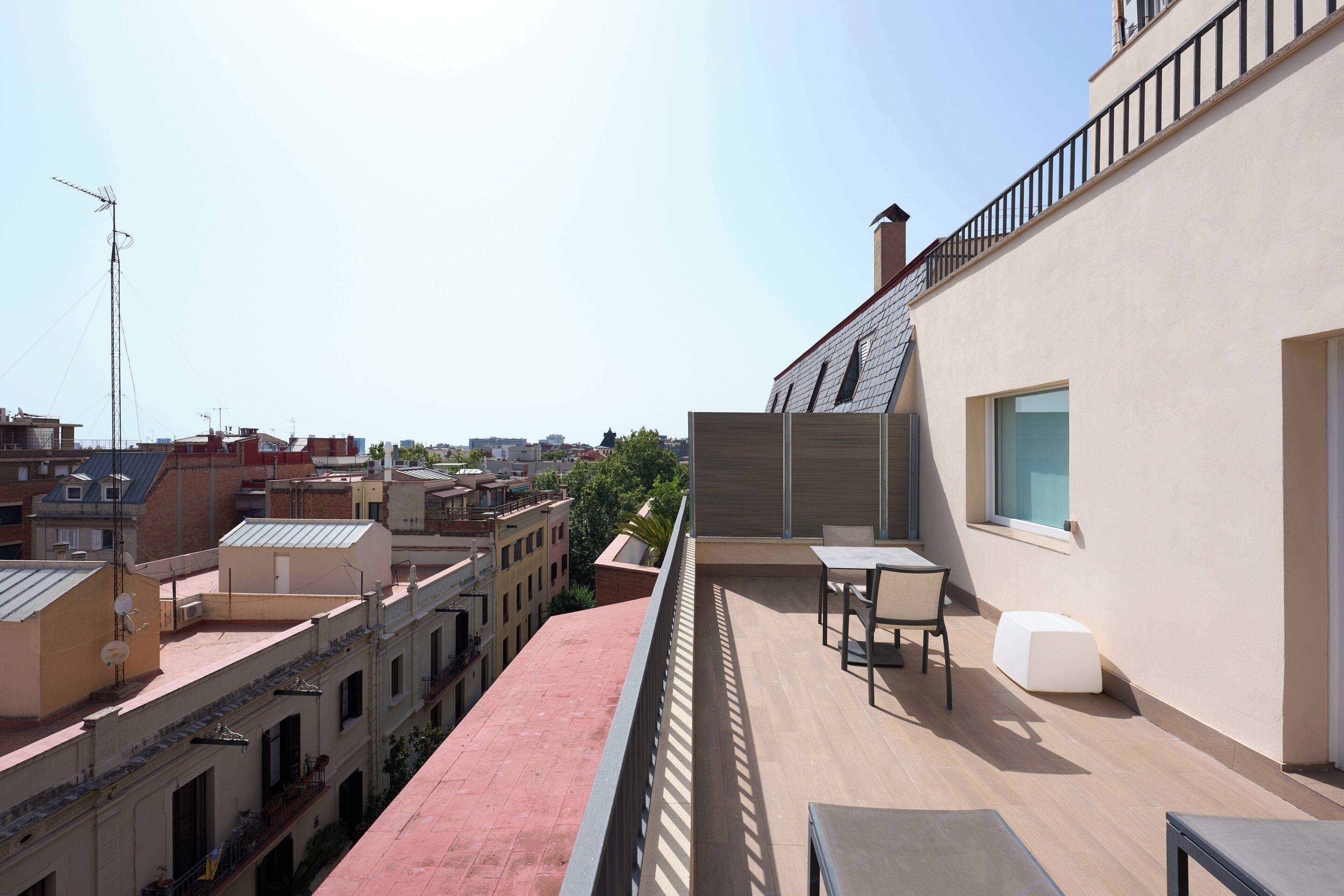 A rooftop terrace with a table and chairs, overlooking a cityscape with various buildings.